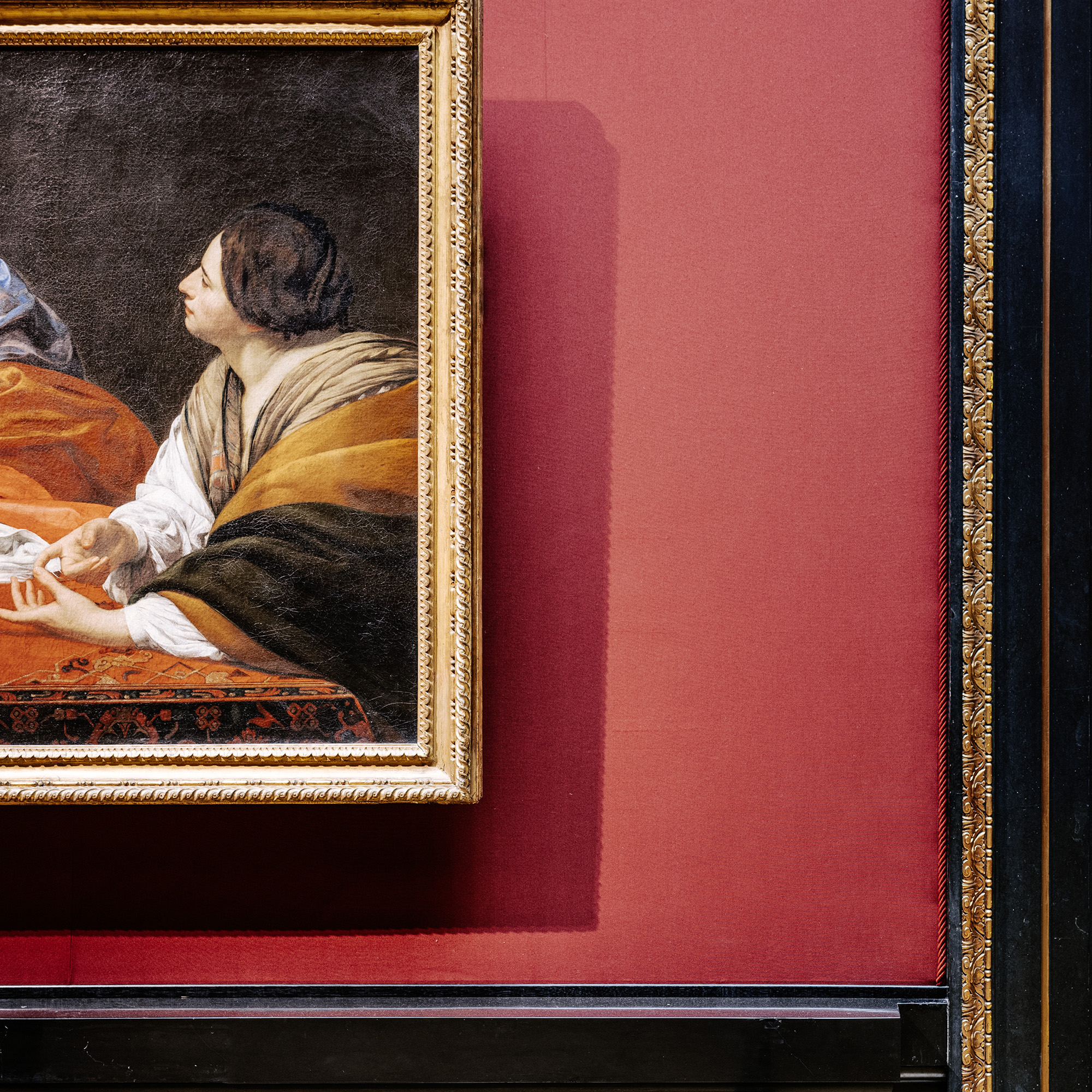 Ausschnitt eines Gemäldes mit einer nach links blickenden Person in historischer Kleidung, kräftige Farbkontraste in Orange, Braun und Weiß, gerahmt in einem vergoldeten Rahmen vor einer weinroten Wandbespannung.