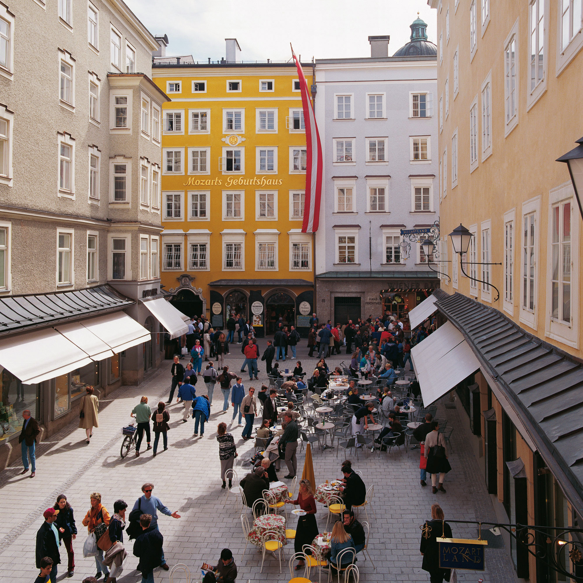 Mozarts Geburtshaus in der Getreidegasse, Salzburg, mit belebtem Platz und Straßencafé.