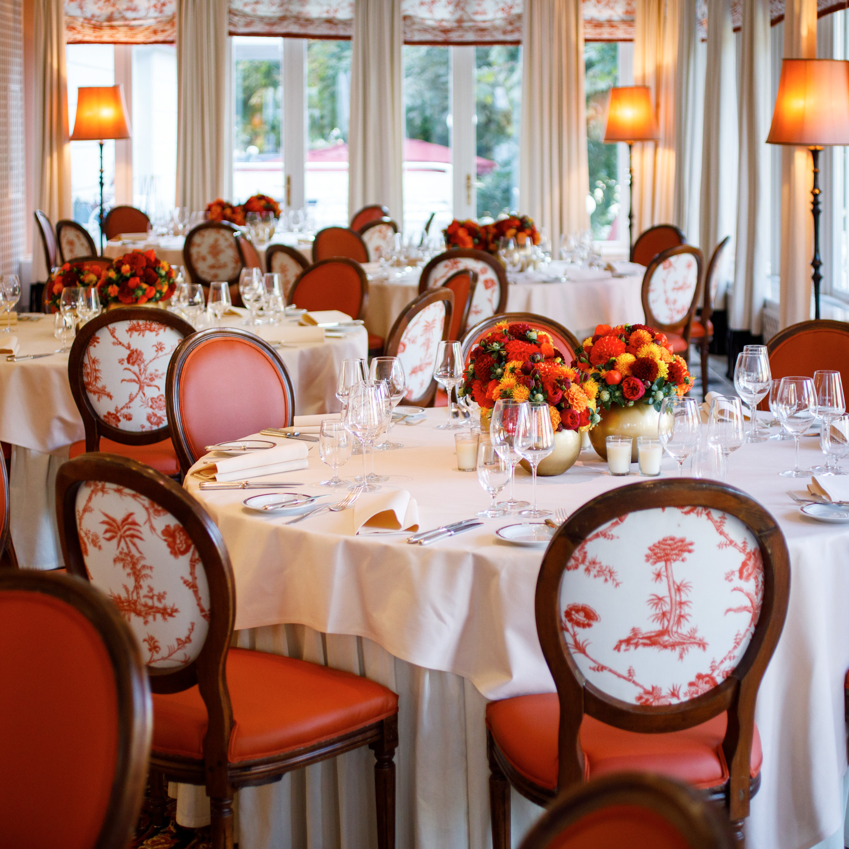 Festlich gedeckter Bankettsaal mit runden Tischen, weißen Tischdecken und kunstvollen Gestecken in warmen Orange- und Rottönen.
