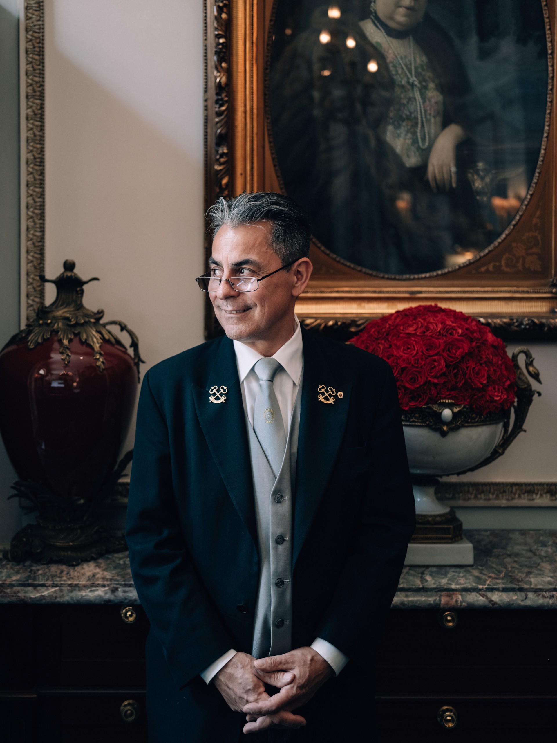 Hotel Sacher Wien, Concierge Ein Concierge in eleganter Uniform mit silbergrauer Weste steht vor einem Gemälde in einem klassisch eingerichteten Raum.