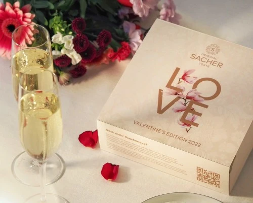 Die Valentins-Edition 2022 der Original Sacher-Torte wird in einer liebevoll gestalteten Verpackung mit floralen Elementen präsentiert – ein stilvoller Ausdruck von Liebe, begleitet von Champagner und Rosenblättern