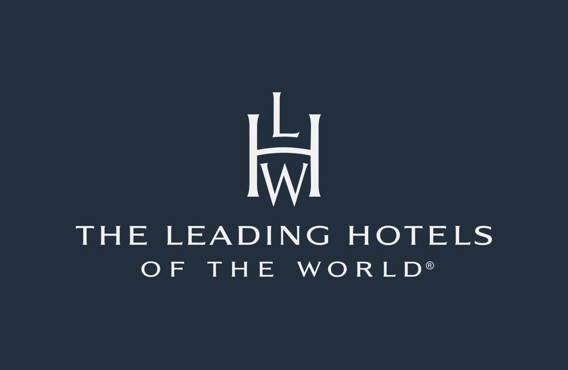 Das Logo von **The Leading Hotels of the World** auf dunkelblauem Hintergrund, bestehend aus einem stilisierten Monogramm „LHW“ und dem darunter gesetzten Schriftzug in eleganter, weißer Typografie.