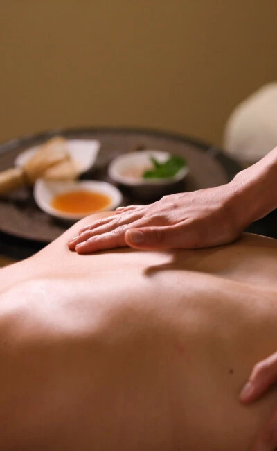 Wellnessanwendung mit entspannender Rückenmassage, im Hintergrund natürliche Pflegeprodukte.