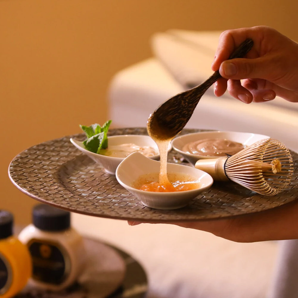 Fein angerichtete Spa-Zutaten in Schälchen, darunter Honig, Cremes und Minze, auf dekorativem Tablett.
