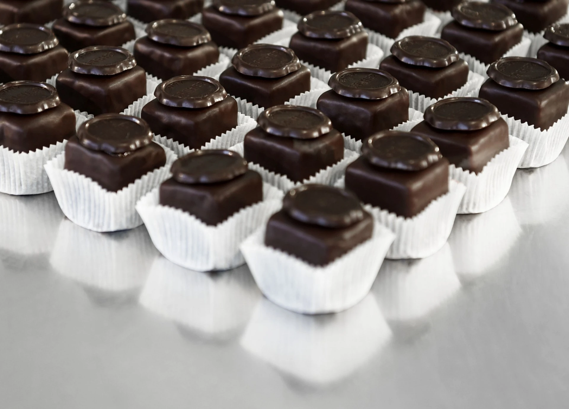 Mehrere Original Sacher-Würfel in ordentlichen Reihen auf silbernem Untergrund arrangiert.