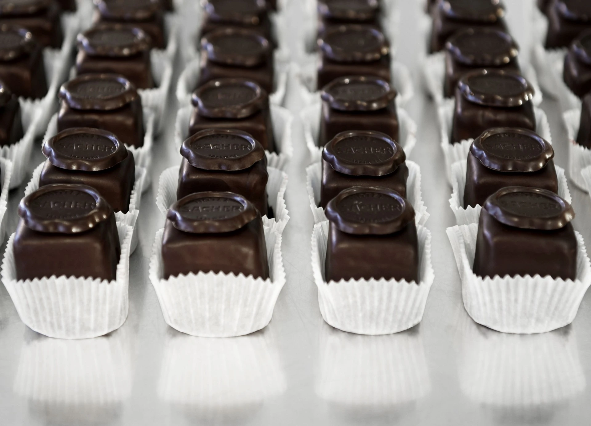 Mehrere Reihen perfekt platzierter Original Sacher-Würfel auf einer glänzenden Oberfläche.