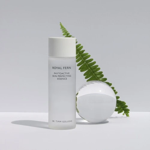 Royal Fern Phytoactive Skin Perfecting Essence elegant arrangiert neben einem Glasball und Farnblatt auf hellem, minimalistischem Hintergrund.