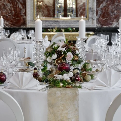 Ein festlich gedeckter runder Tisch mit weißer Tischdecke, eleganten Gläsern und weihnachtlicher Dekoration.