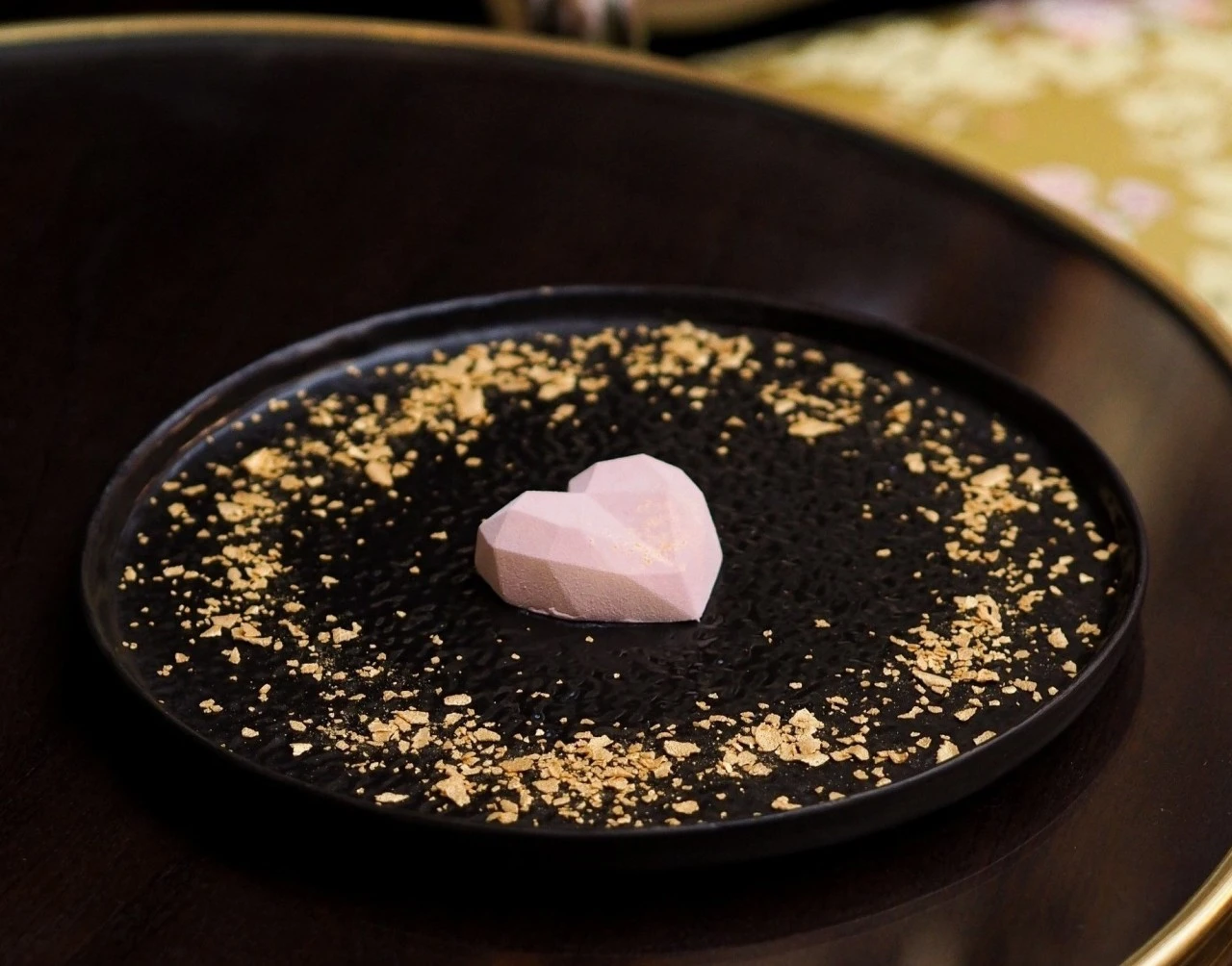 Ein kleines Kunstwerk auf einem Teller: Im Zentrum dieser eleganten Komposition liegt ein geometrisch geformtes, rosafarbenes Herz