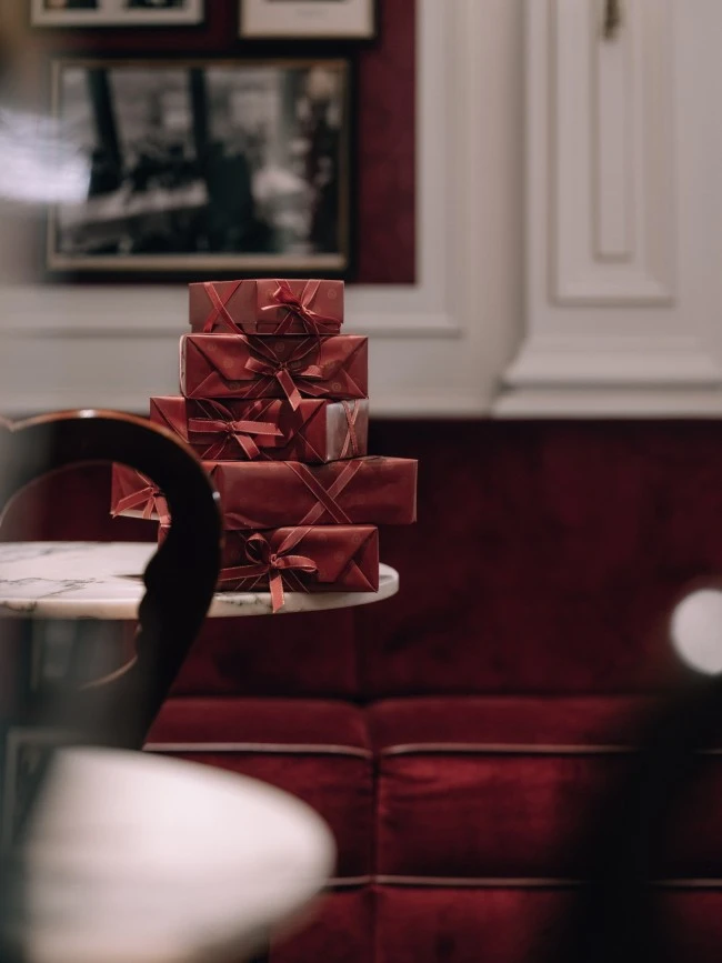 Ein eleganter Marmortisch im klassischen Ambiente des Hotel Sacher ist mit einer kunstvoll arrangierten Pyramide aus burgunderroten Geschenkboxen dekoriert.