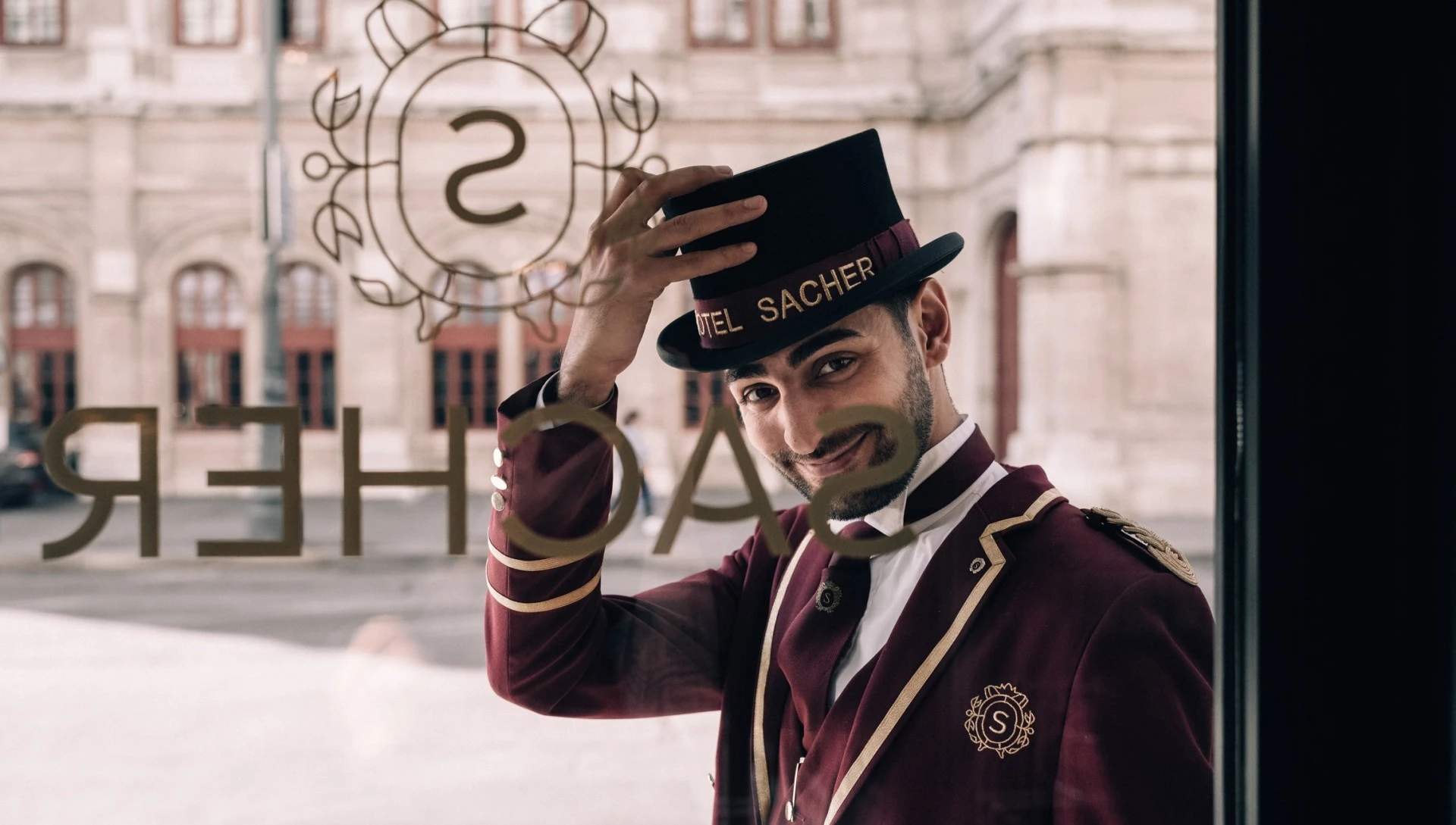 Ein Portier des Hotel Sacher grüßt freundlich mit einem Lächeln und hebt stilvoll seinen Zylinder