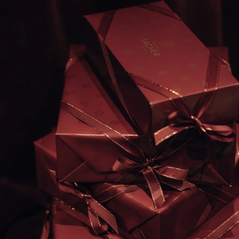 Verpackung der Original-Sachertorte Stilvoll in bordeauxrotes Papier gehüllt, verziert mit feinen Schleifen und dezentem Sacher-Logo