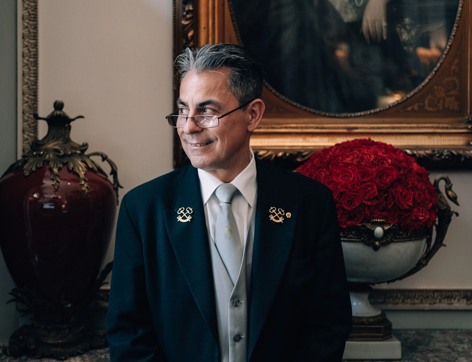 Ein Concierge steht elegant vor einem Tisch mit einer opulenten roten Rosenkugel in einer edlen Vase.