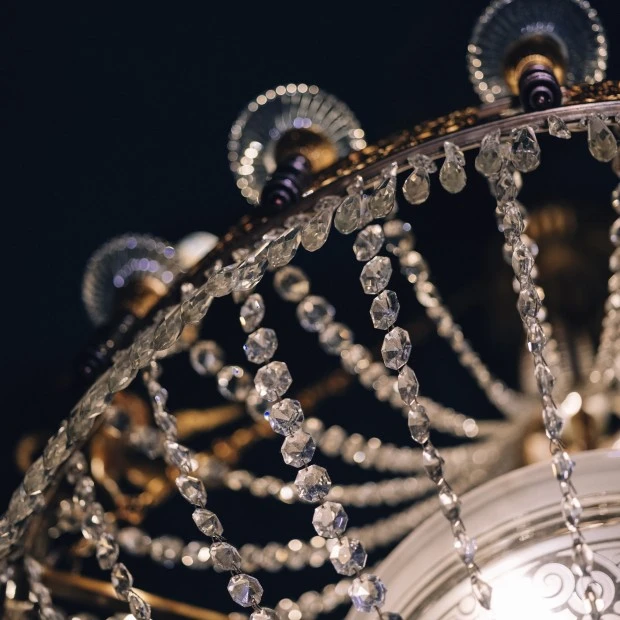 Ein prächtiger Kristallluster, eingefangen in einer Nahaufnahme: filigran geschliffene Kristallketten funkeln im warmen Licht, kunstvoll arrangiert an einem vergoldeten Rahmen.