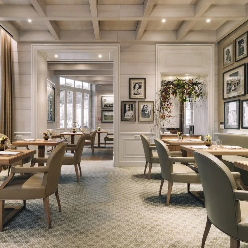 Ein elegantes Restaurant mit hellen Holztischen und bequemen, gepolsterten Stühlen. Die Einrichtung wirkt modern und dennoch klassisch. An den Wänden hängen zahlreiche Schwarz-Weiß-Porträts berühmter Persönlichkeiten.