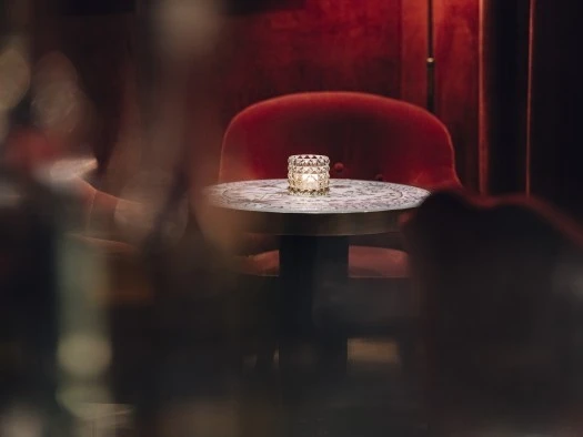 Hotel Sacher Salzburg, Sacher Bar Ein runder Marmortisch mit feiner Maserung steht im Mittelpunkt, umgeben von eleganten, samtroten Polstersesseln. Auf dem Tisch steht ein dekoratives Teelichtglas, das eine warme, gemütliche Stimmung erzeugt. Die gedämpfte Beleuchtung und samtbezogenen Wände im Hintergrund verleihen dem Raum eine intime, luxuriöse Atmosphäre.