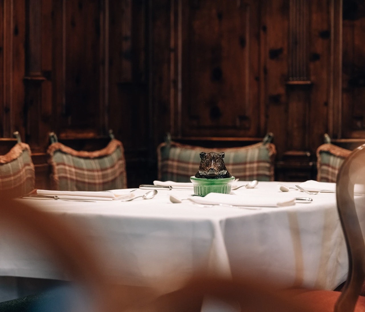 Gedeckter Holztisch in einem traditionell eingerichteten Restaurant. Im Hintergrund sind karierte Sitzkissen vor einer rustikalen Holzvertäfelung zu sehen, die dem Raum eine gemütliche, alpenländische Atmosphäre verleihen.