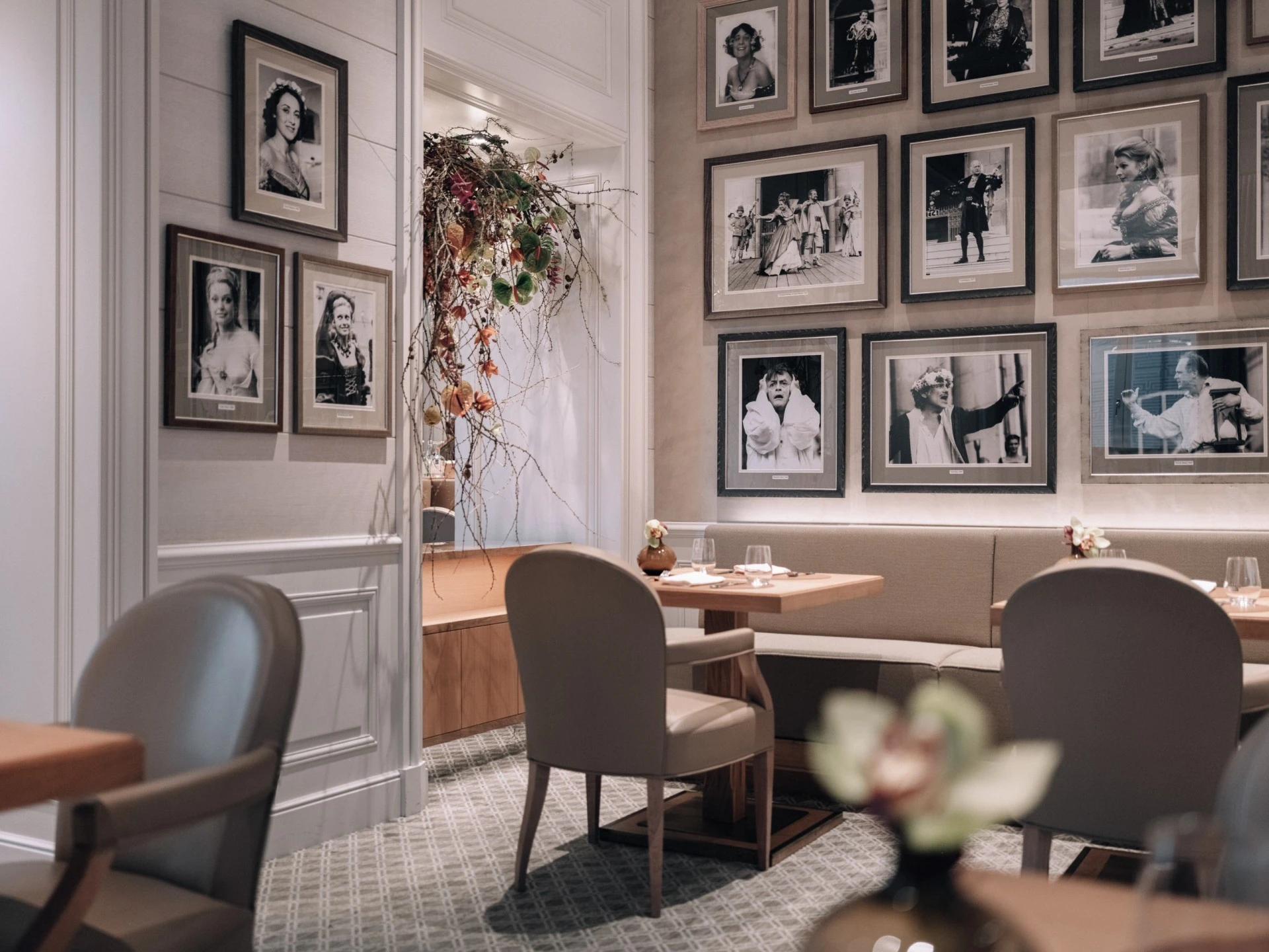 Elegantes Restaurant mit gemütlicher Atmosphäre. An den Wänden hängen zahlreiche Schwarz-Weiß-Porträts prominenter Persönlichkeiten, überwiegend aus Kunst und Kultur. Die Einrichtung ist geprägt von warmen Holztönen, bequemen Polsterstühlen und stilvoll gedeckten Tischen.