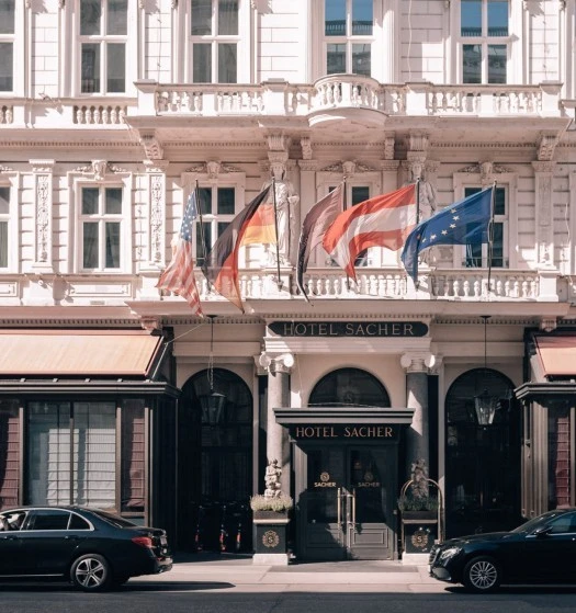 Hotel Sacher Wien, Gebäude Der Haupteingang des Hotel Sacher Wien mit einem eleganten Eingangsbereich, flankiert von Säulen und dekorativen Pflanzgefäßen.