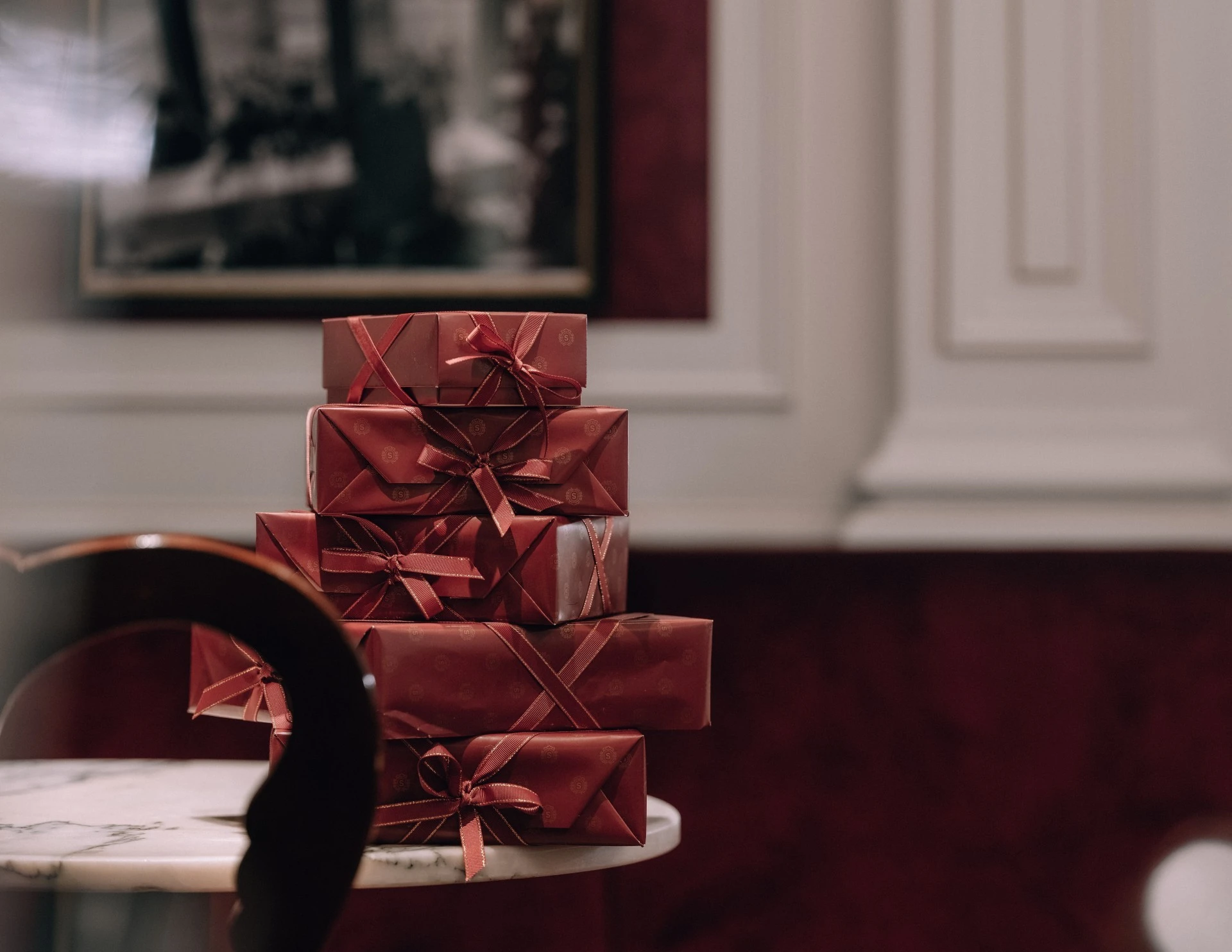 Auf dem Bild sind mehrere edle Verpackungen der Original Sacher-Torte zu sehen. Sie sind in typischem Sacher-Rot gehalten, mit feinen Mustern versehen und mit eleganten Schleifen verziert. Die Verpackungen sind sorgfältig gestapelt und vermitteln einen hochwertigen, traditionellen Eindruck.