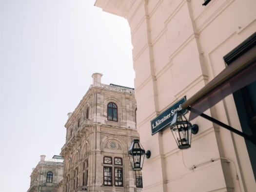 Hotel Sacher Wien, Standort Wiener Staatsoper. Im Vordergrund ist ein Straßenschild mit der Aufschrift „Kärntner Straße“ zu sehen.