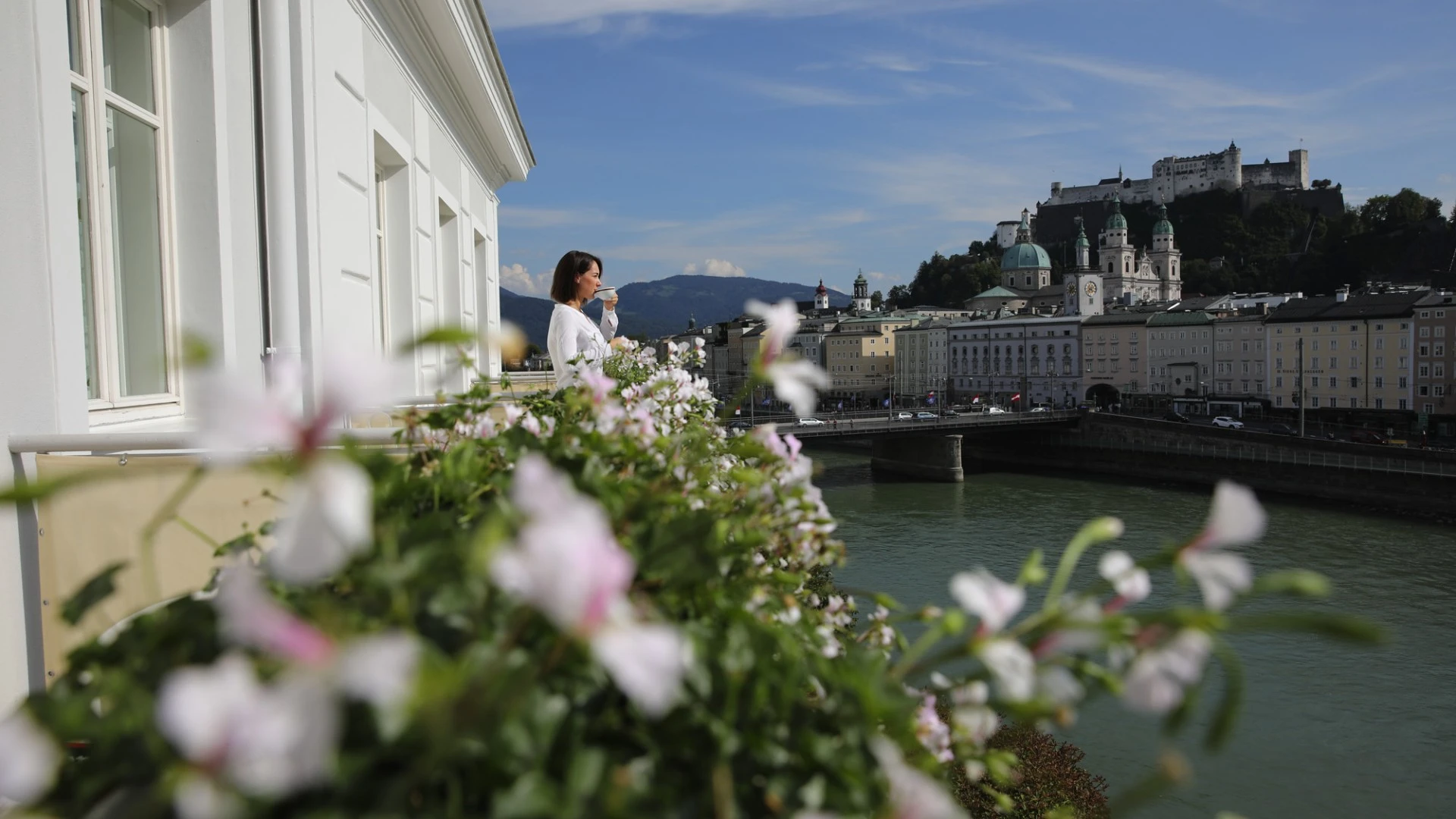Terrasse mit Blumenbepflanzung und Blick auf Salzburgs Altstadt und Festung, Frau genießt Kaffee.