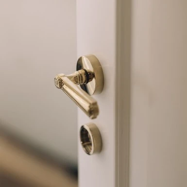 Ein Türgriff aus glänzendem Messing mit feinen Verzierungen an einer weißen Tür.