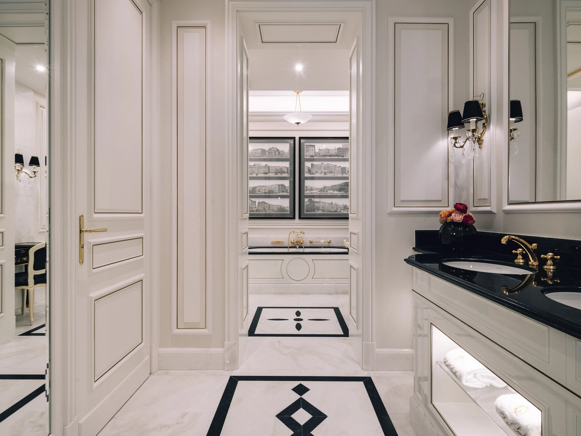 Elegantes Badezimmer mit schwarzer Marmor-Doppelwaschtischplatte, goldenen Armaturen und weißen Handtüchern. Im Hintergrund eine freistehende Badewanne vor historischen Stadtansichten und stilvoller Wand- und Bodengestaltung in Schwarz-Weiß.