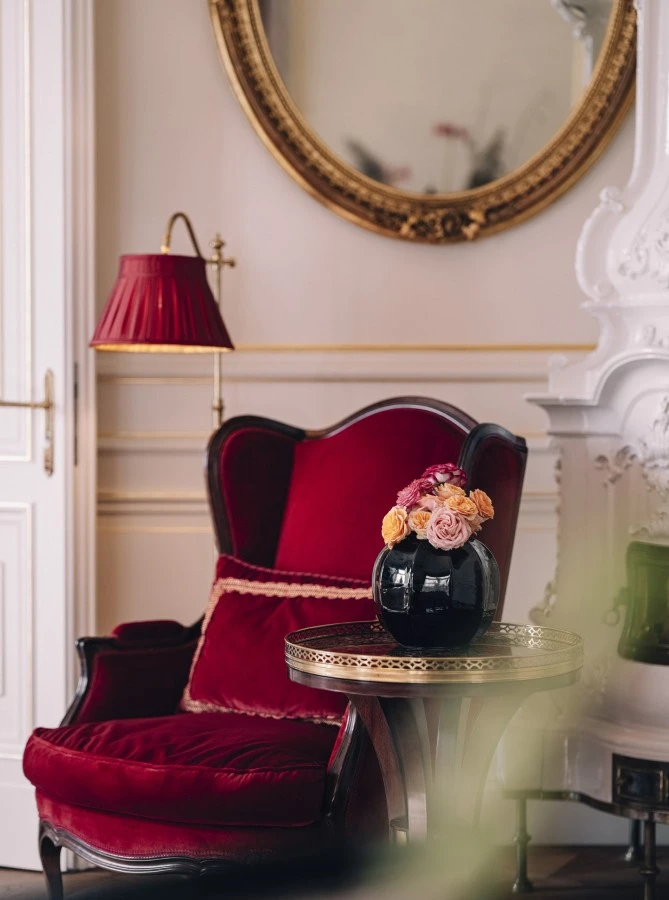 Philharmoniker Suite, Hotel Sacher Wien, Grande Signature Suite, Luxus, Wien, 5-Sterne, Hotel Ein edler roter Sessel steht neben einem kleinen Holztisch mit goldenen Details. Darauf eine schwarze Vase mit frischen Rosen in zarten Farben. Die Umgebung wirkt klassisch und stilvoll.