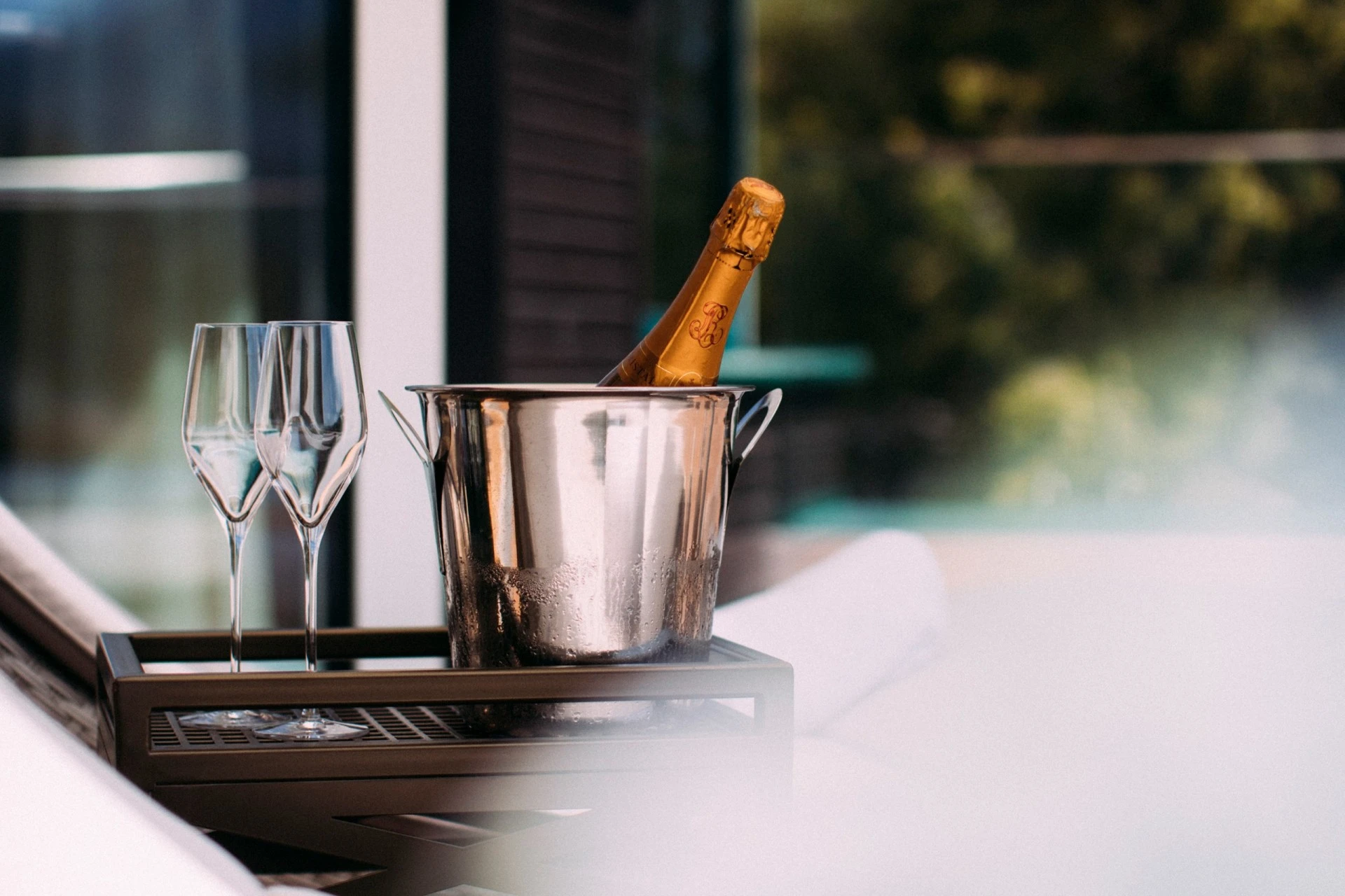 Zwei Sektgläser und eine gekühlte Flasche Champagner in einem silbernen Eiskübel auf einem Tablett – bereit für einen besonderen Moment.