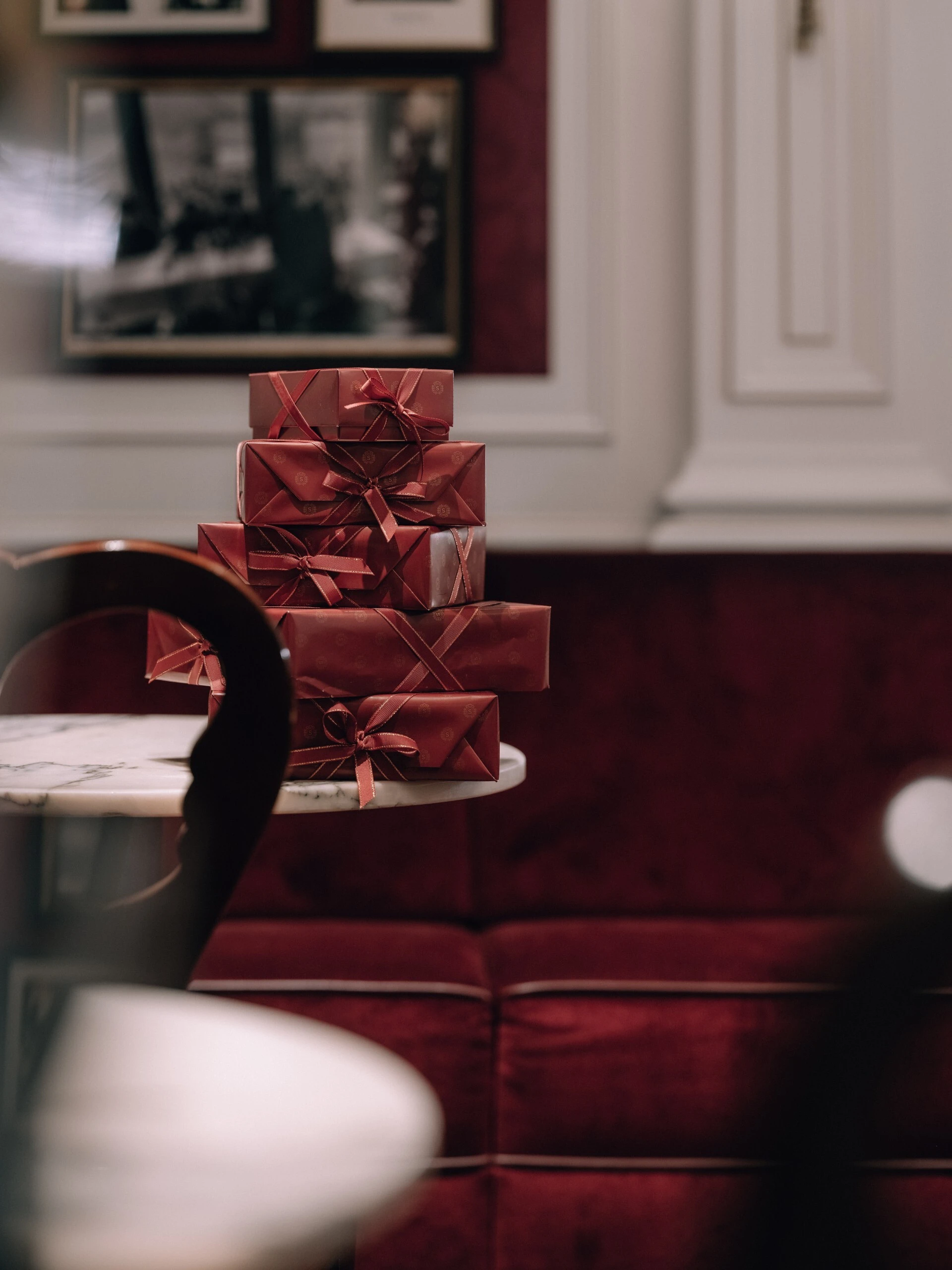 Mehrere edle Holzschachteln, in denen sich die Original Sacher-Torte befindet, sind übereinandergestapelt auf einem kleinen Marmortisch arrangiert. Die Schachteln sind in rotem Papier mit passenden Schleifen verpackt.