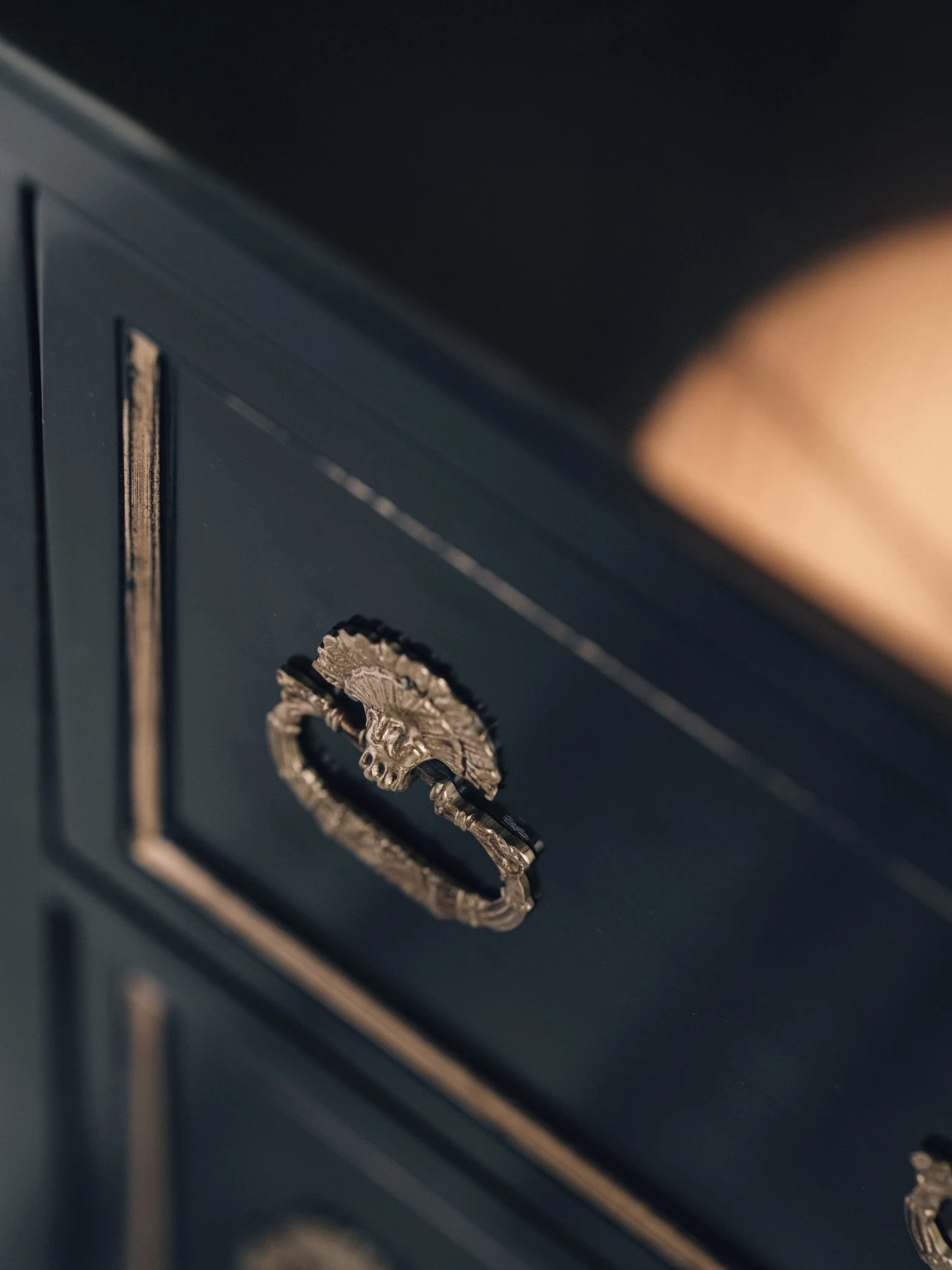 Detailaufnahme eines antiken, messingfarbenen Möbelgriffs in Form eines Löwenkopfs mit Ring an einem dunkel lackierten Holzschrank.