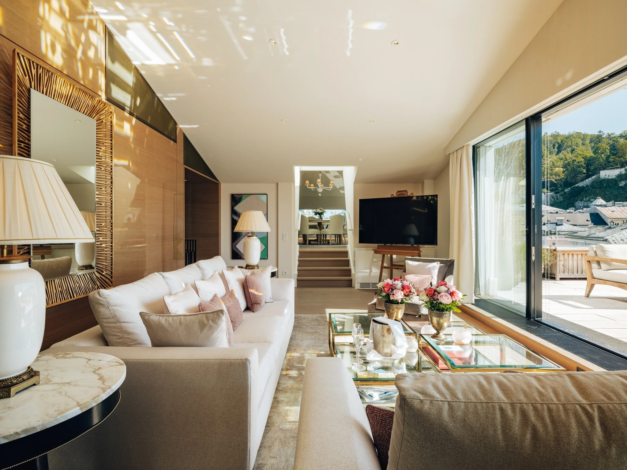 Lichtdurchflutete Sky Suite mit eleganter Sitzecke, pastellfarbenen Kissen, frischen Blumenarrangements auf dem Couchtisch und direktem Zugang zur großzügigen Terrasse mit Blick über die Stadt Salzburg.