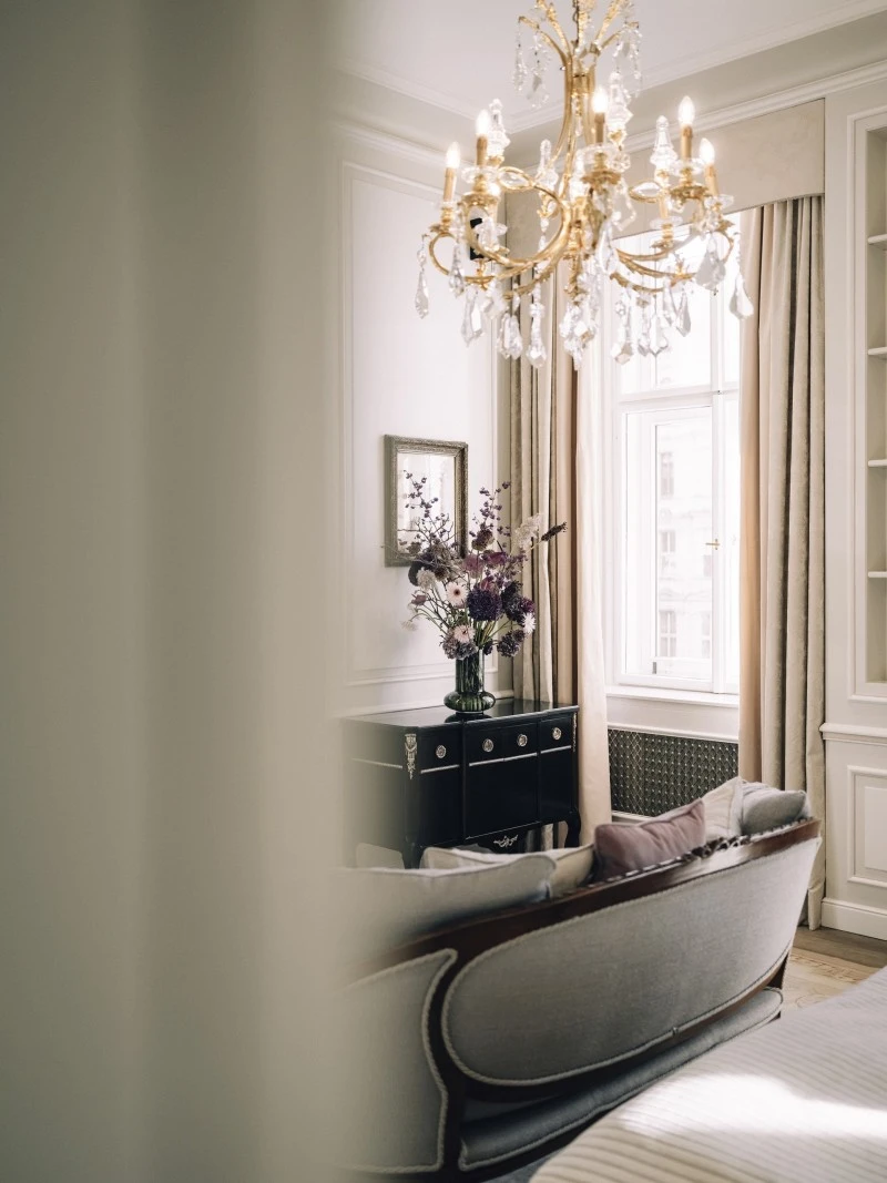 Ausschnitt der Signature Suite mit einem Kristallluster, einer klassischen Sitzbank und einer Kommode mit frischem Blumenarrangement vor dem Fenster