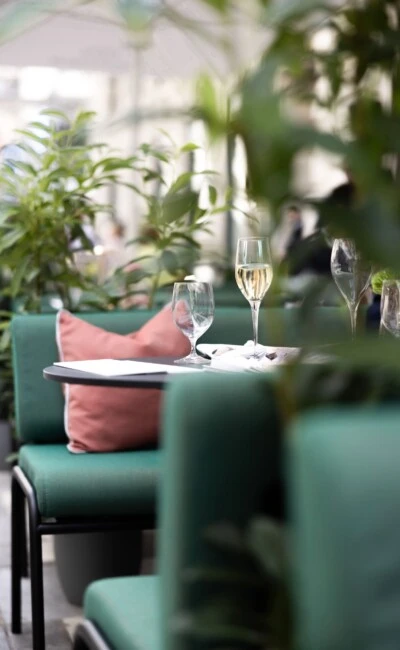 Ein Blick auf den Sommergarten des Hotel Sacher Wien mit grün gepolsterten Sitzmöbeln, roséfarbenen Kissen und elegant gedecktem Tisch