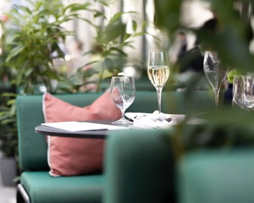 Ein Blick auf den Sommergarten des Hotel Sacher Wien mit grün gepolsterten Sitzmöbeln, roséfarbenen Kissen und elegant gedecktem Tisch