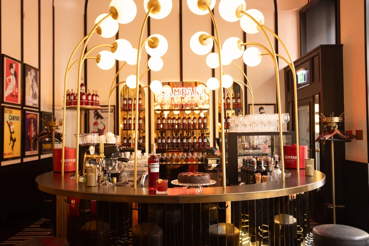 Stylische Bar im Sacher Salon mit goldenen Lampen, Campari-Flaschen und Original Sacher Torte
