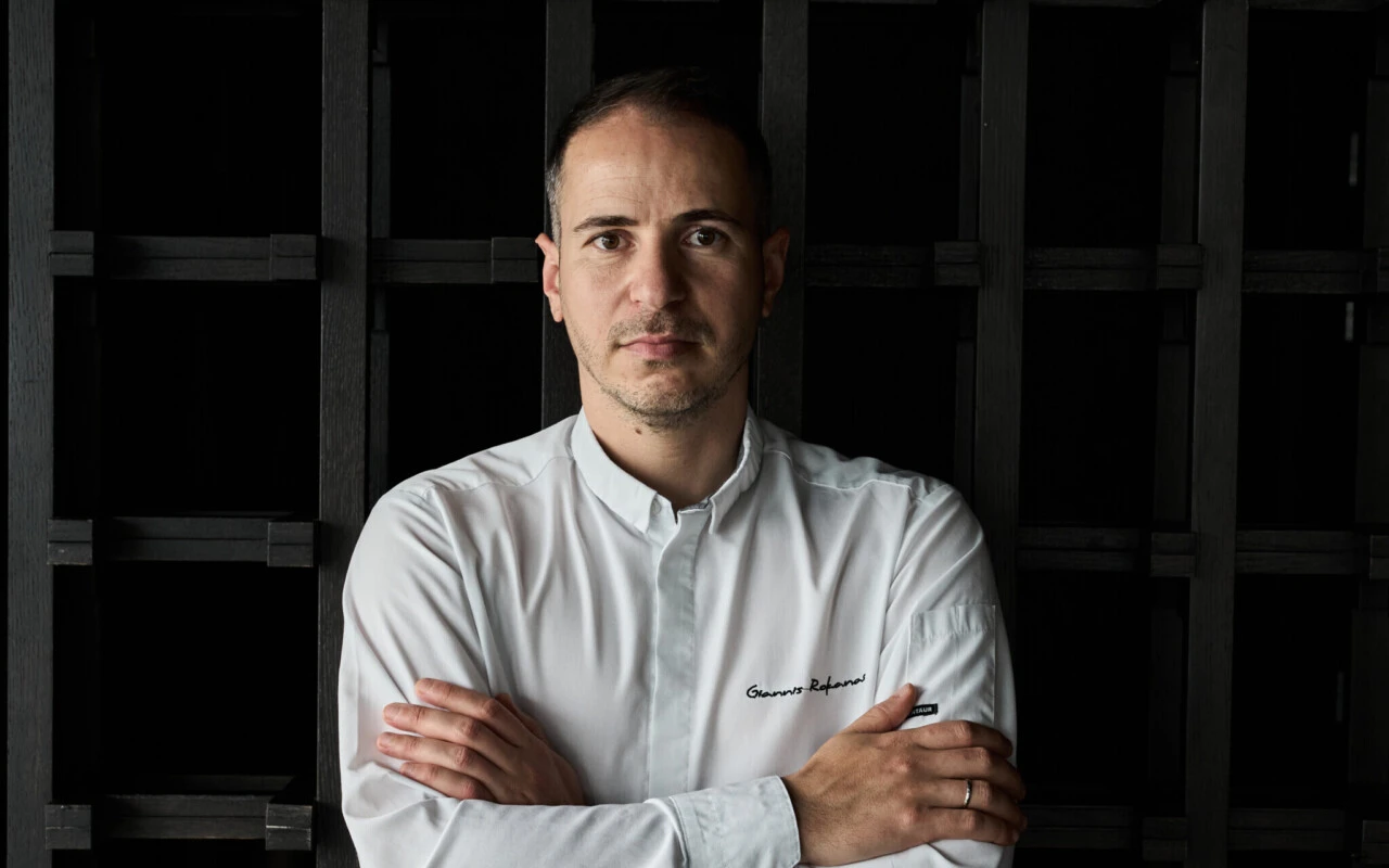Chef Giannis Rokanas steht mit geschränkten Händen vor einer Wand