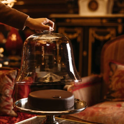 Original Sacher-Torte auf einer silbernen Tortenplatte, die gerade unter einer Glasglocke hervorgehoben wird - in der Lobby Hotel Sacher Wien