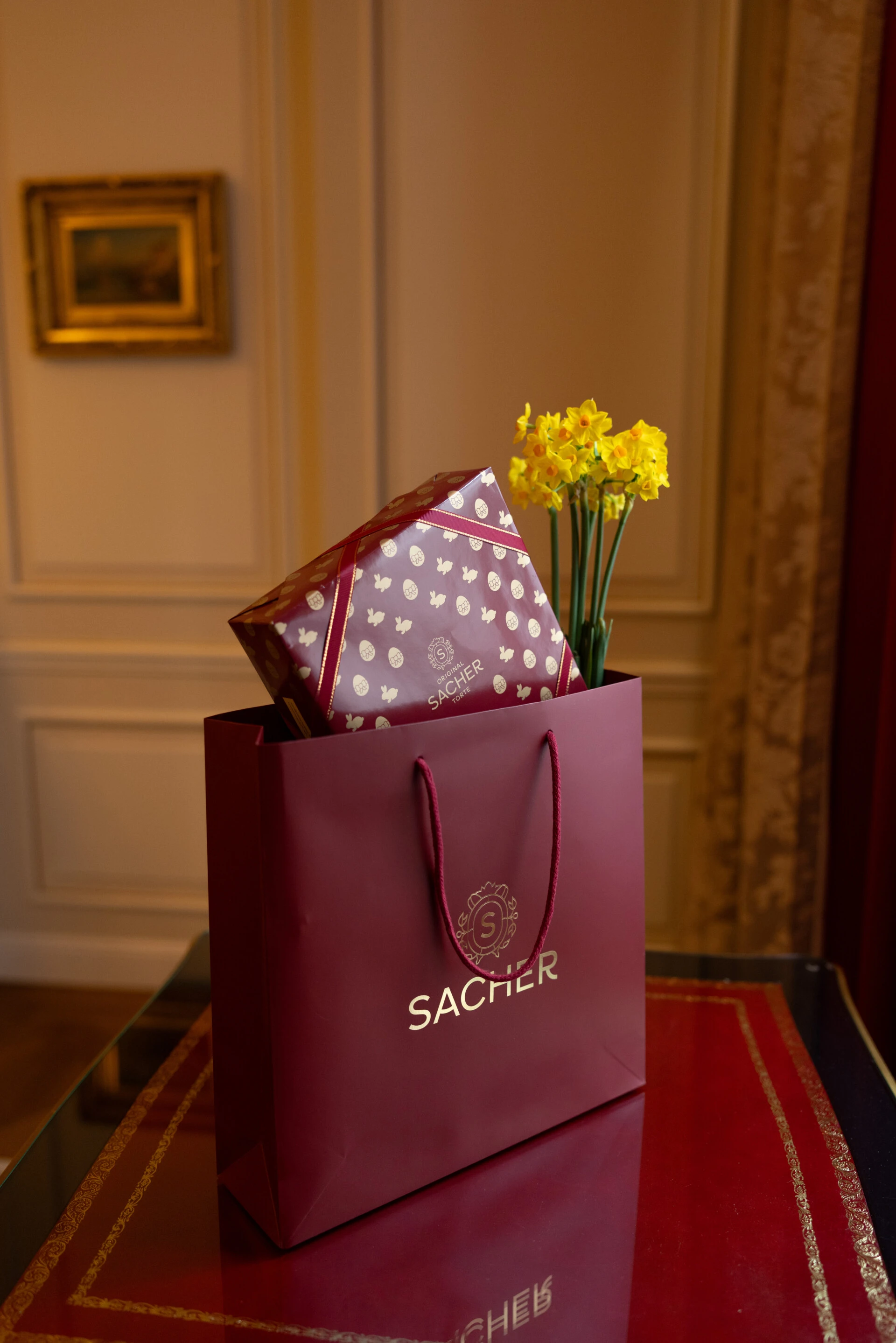 Original Sacher-Torte Osteredition in der roten Sacher-Kartonverpackung neben gelben Blumen