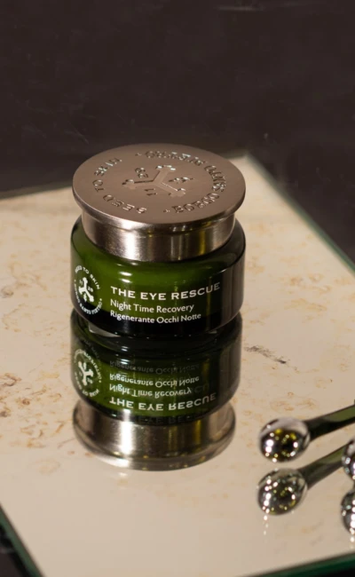 Grüner Tiegel „The Eye Rescue“ mit silbernem Deckel auf einem Spiegel, daneben zwei metallische Applikatoren.