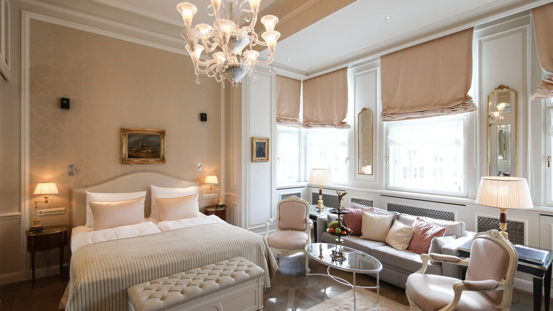 Lichtdurchflutetes Schlafzimmer in sanften Creme- und Rosétönen mit Kronleuchter, Sitzgruppe und klassischem Dekor.