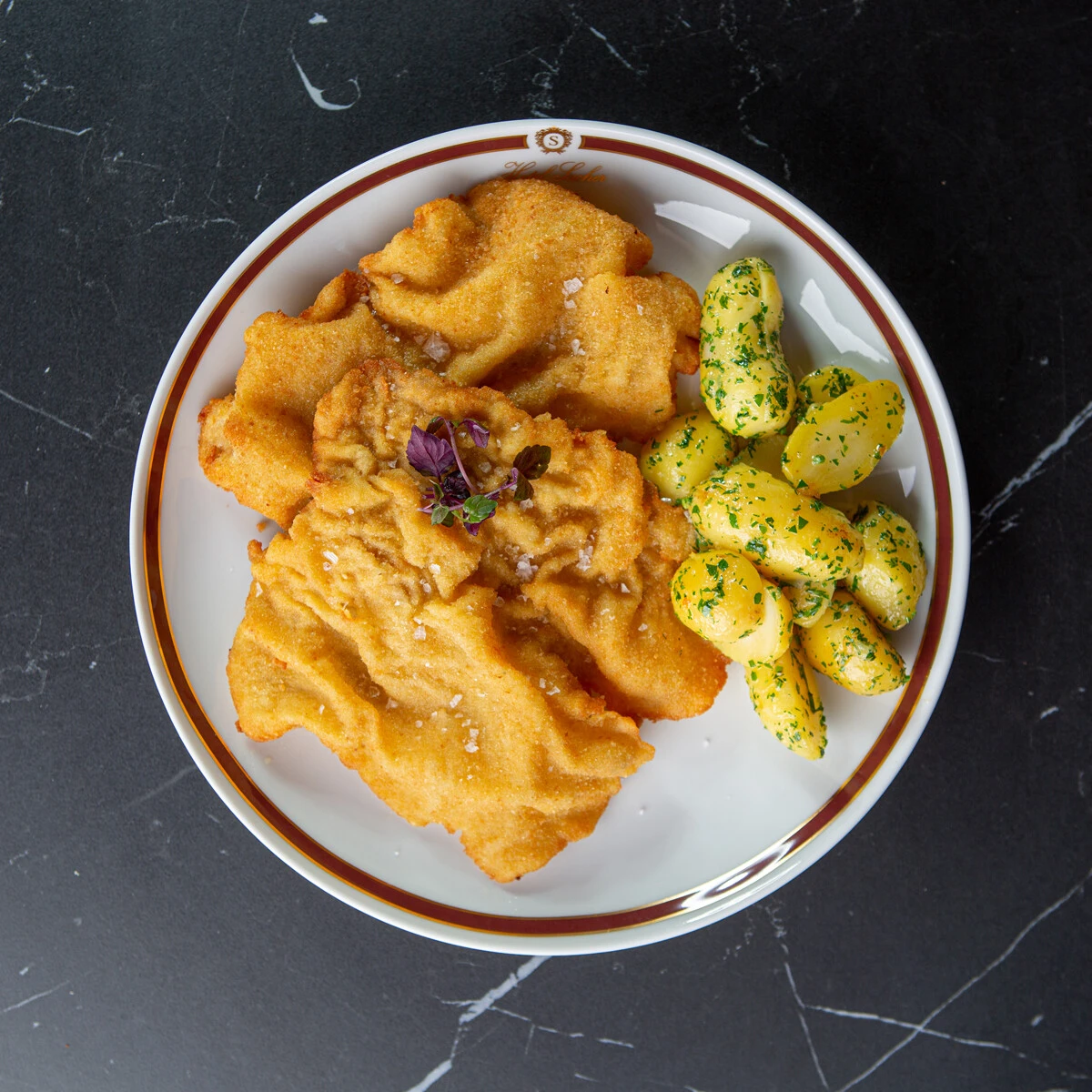 Goldbraunes Wiener Schnitzel mit Petersilienkartoffeln – klassisch, knusprig und elegant auf Sacher-Porzellan serviert.