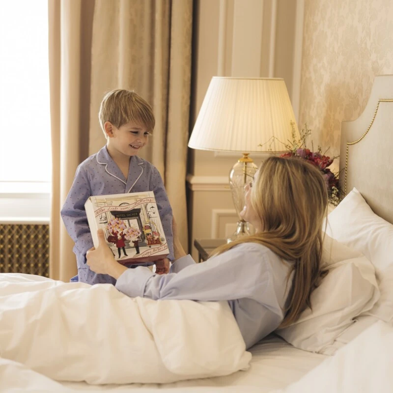 Mutter und Kind genießen einen entspannten Moment im Bett – beide in Pyjamas, mit der Muttertagsedition von der Original Sacher-Torte
