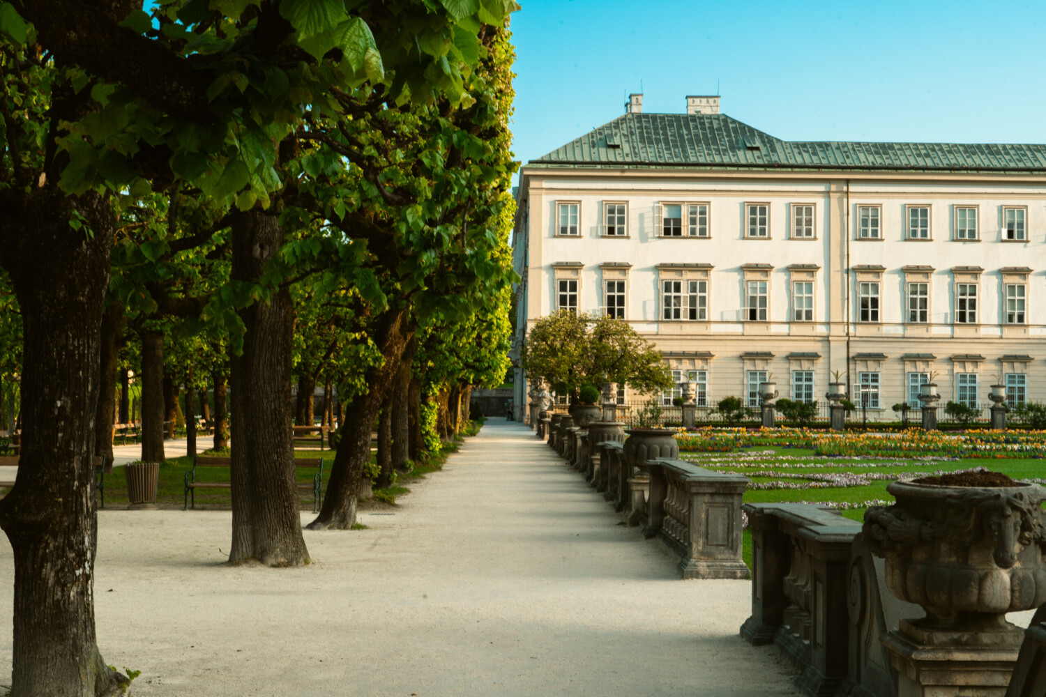 Die linke Seite von Schloss Mirabell, umgeben von Bäumen und einem blauen Himmel.