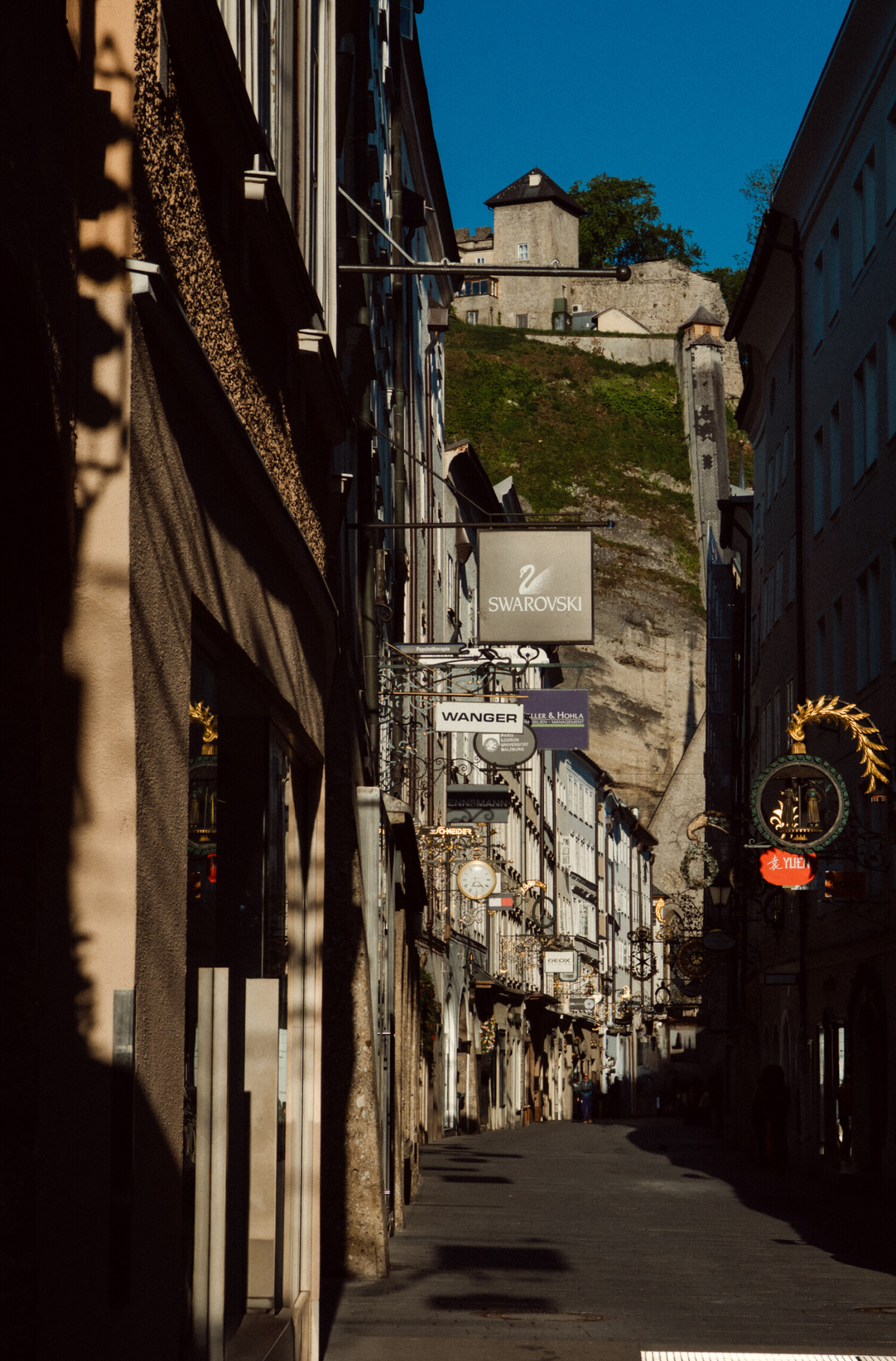 Eine Straße in der Altstadt von Salzburg mit Geschäftsschildern, die aus den Läden ragen.