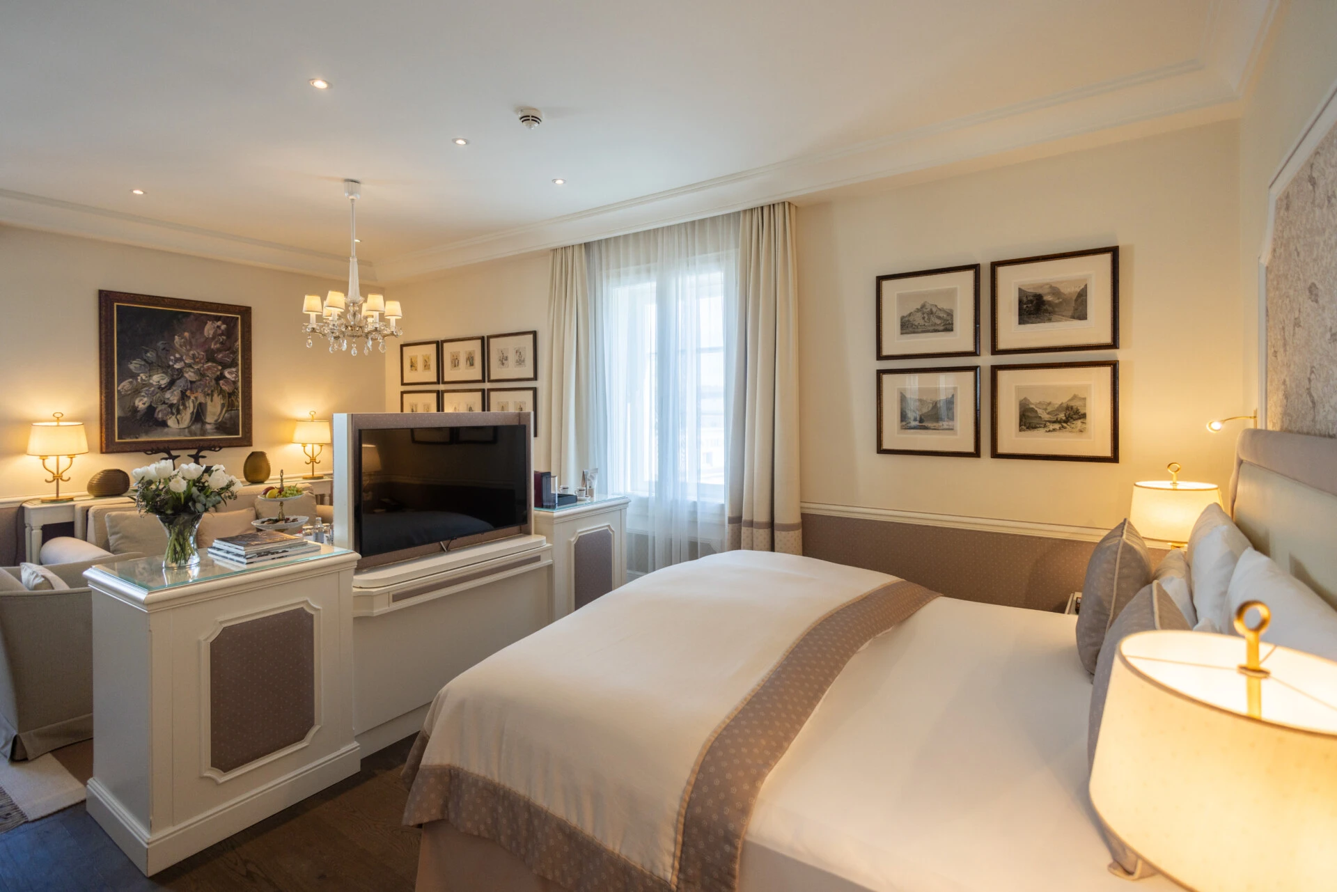 Geräumige Hotelsuite im Hotel Sacher mit Kingsize-Bett, gemütlicher Sitzecke und TV-Konsole vor dem Bett