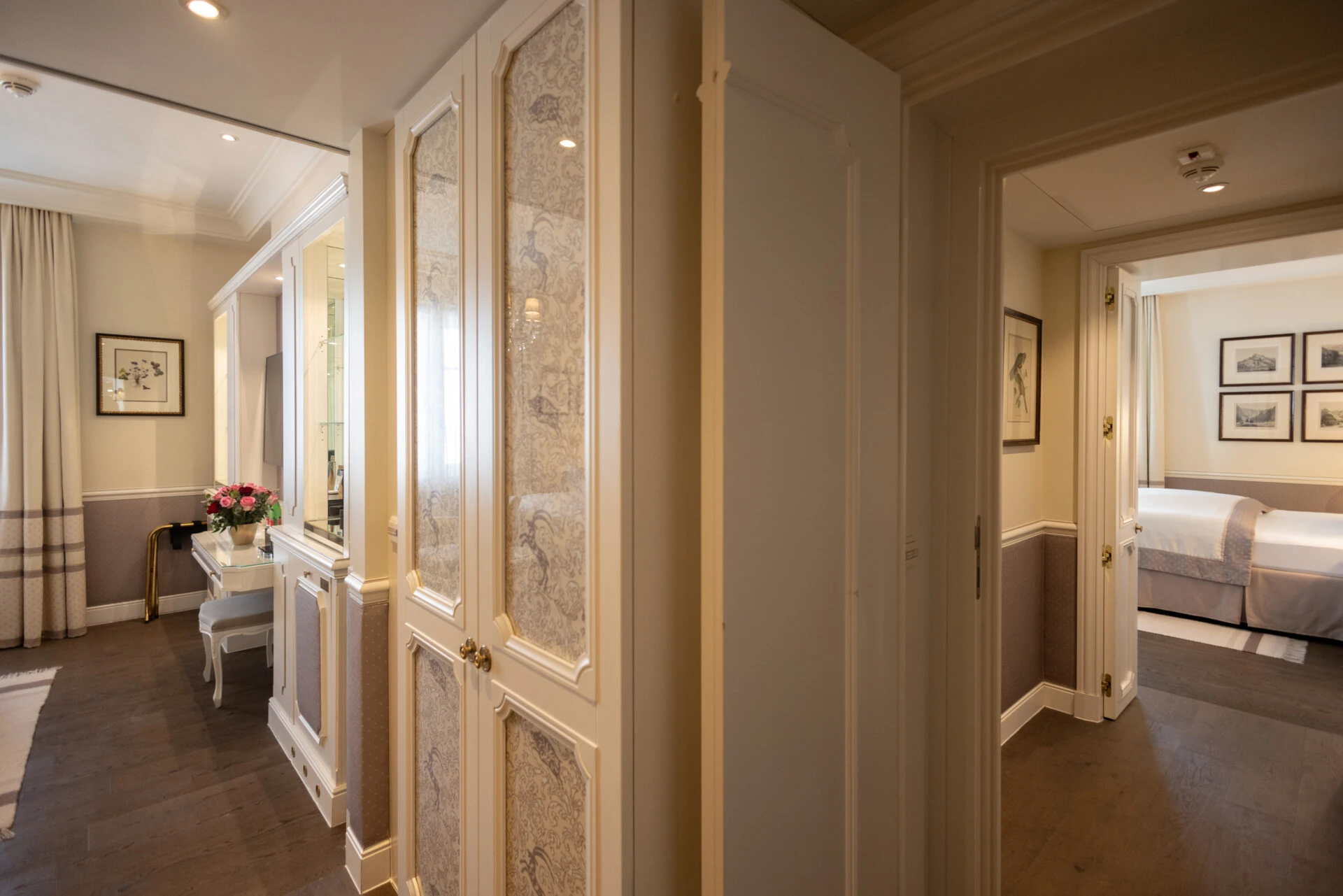 Heller, eleganter Flur mit edlen Holzböden, kunstvoll verzierten Türen und stilvoll eingerichteten Zimmern. Verbindungsgang in der Suite des Hotel Sacher mit Einbauschrank, Schminktisch und Zugang zum zweiten Schlafzimmer
