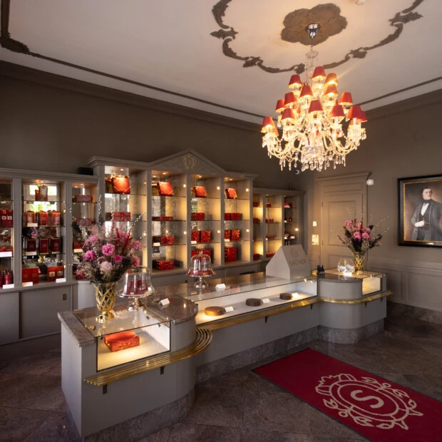 Confiserie Sacher Salzburg - Exklusive Boutique mit elegant präsentierten Original Sacher-Torten, roten Geschenkboxen und stilvollen Blumendekorationen.