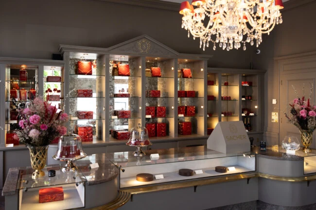Confiserie Sacher Salzburg - Exklusive Boutique mit elegant präsentierten Original Sacher-Torten, roten Geschenkboxen und stilvollen Blumendekorationen.